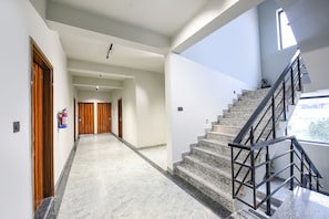 A modern hotel hallway with a marble floor, wooden doors, and a staircase with metal railings. - Fabhotel Naina Residency (Rishikesh)