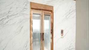 A marble wall with a wooden-framed door and a digital elevator control panel. - Fabhotel Ip Indrapuram (Ghaziabad)