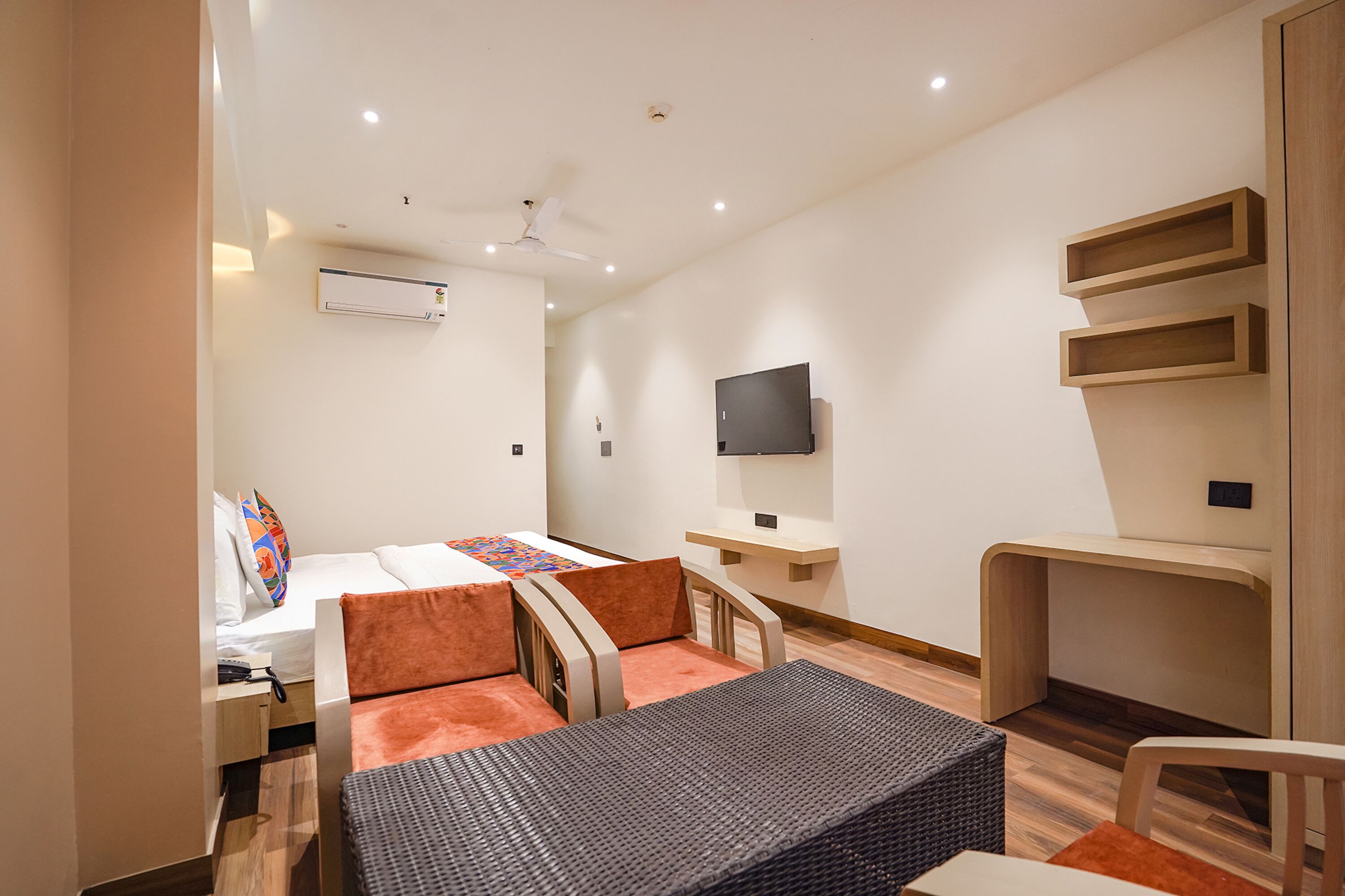 A modern hotel room with a bed, a desk, a chair, a TV, and an air conditioning unit.