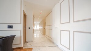 A hallway with a wicker chair, marble flooring, and framed wall panels. - Fabhotel Ip Indrapuram (Ghaziabad)