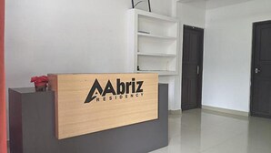 A reception desk with a wooden finish and the logo 'Abriz Residency'. There are white shelves above the desk and a dark door in the background. - Fabexpress Aabriz Residency (Kanayannur)