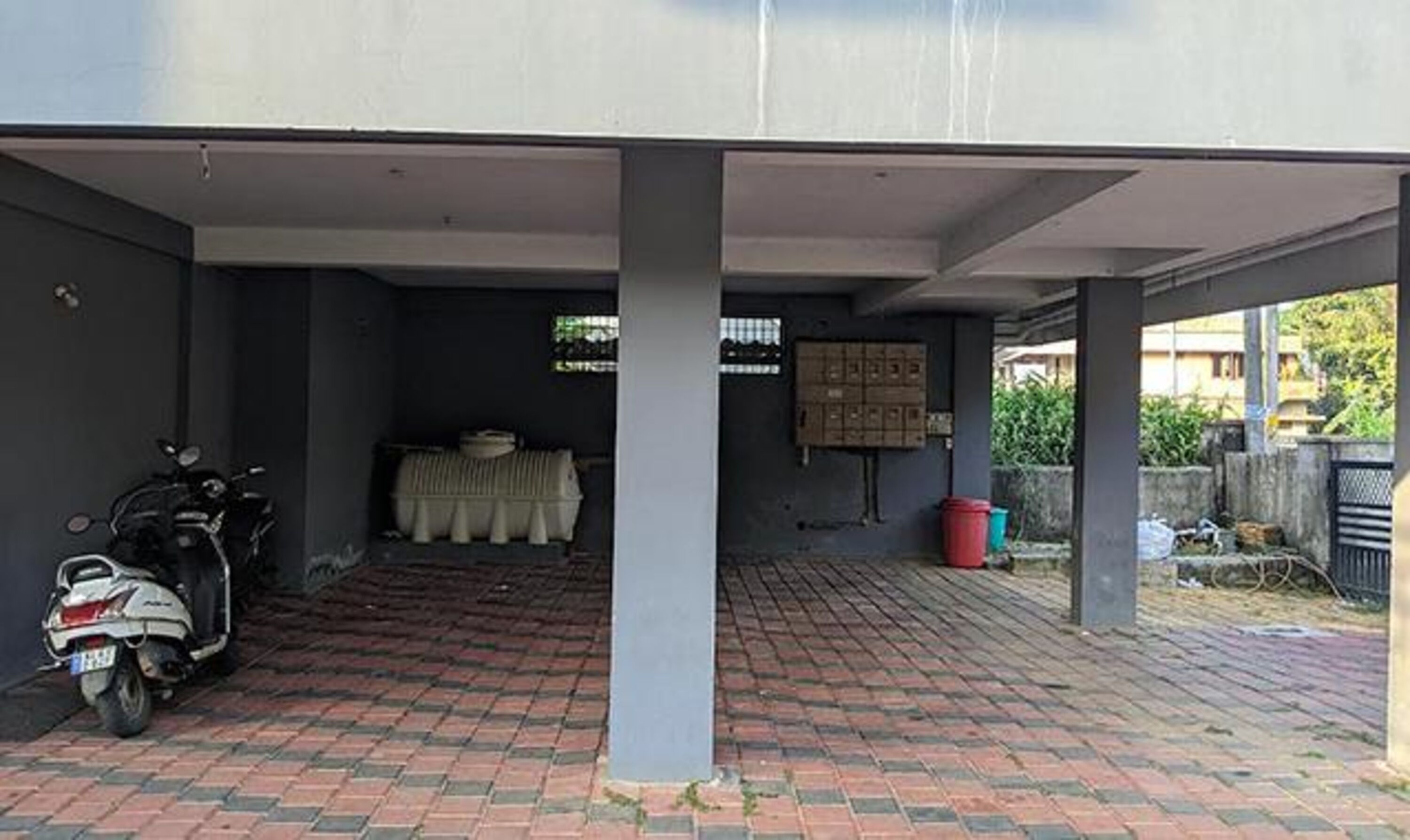 A covered parking area with a scooter parked on the left, a brick floor, and a covered seating area with a table and chairs in the center.