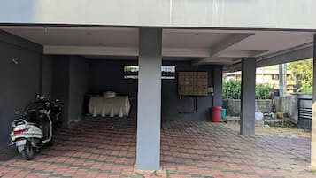 A covered parking area with a scooter parked on the left, a brick floor, and a covered seating area with a table and chairs in the center.