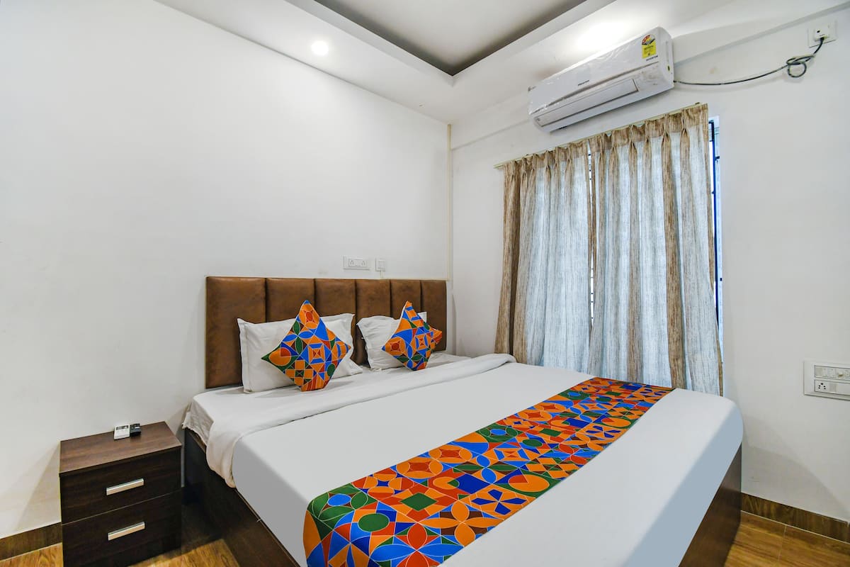 Quarto de hotel com cama, mesa de cabeceira, tomada e aparelho de ar condicionado.