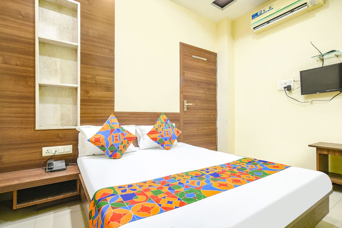 Habitación de hotel con cama, armario de madera, estantería, televisor y aire acondicionado.