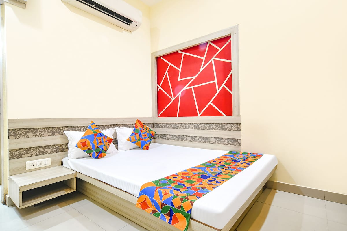 Una cama bien hecha con un colorido mantón geométrico, una almohada blanca y una almohada multicolora.