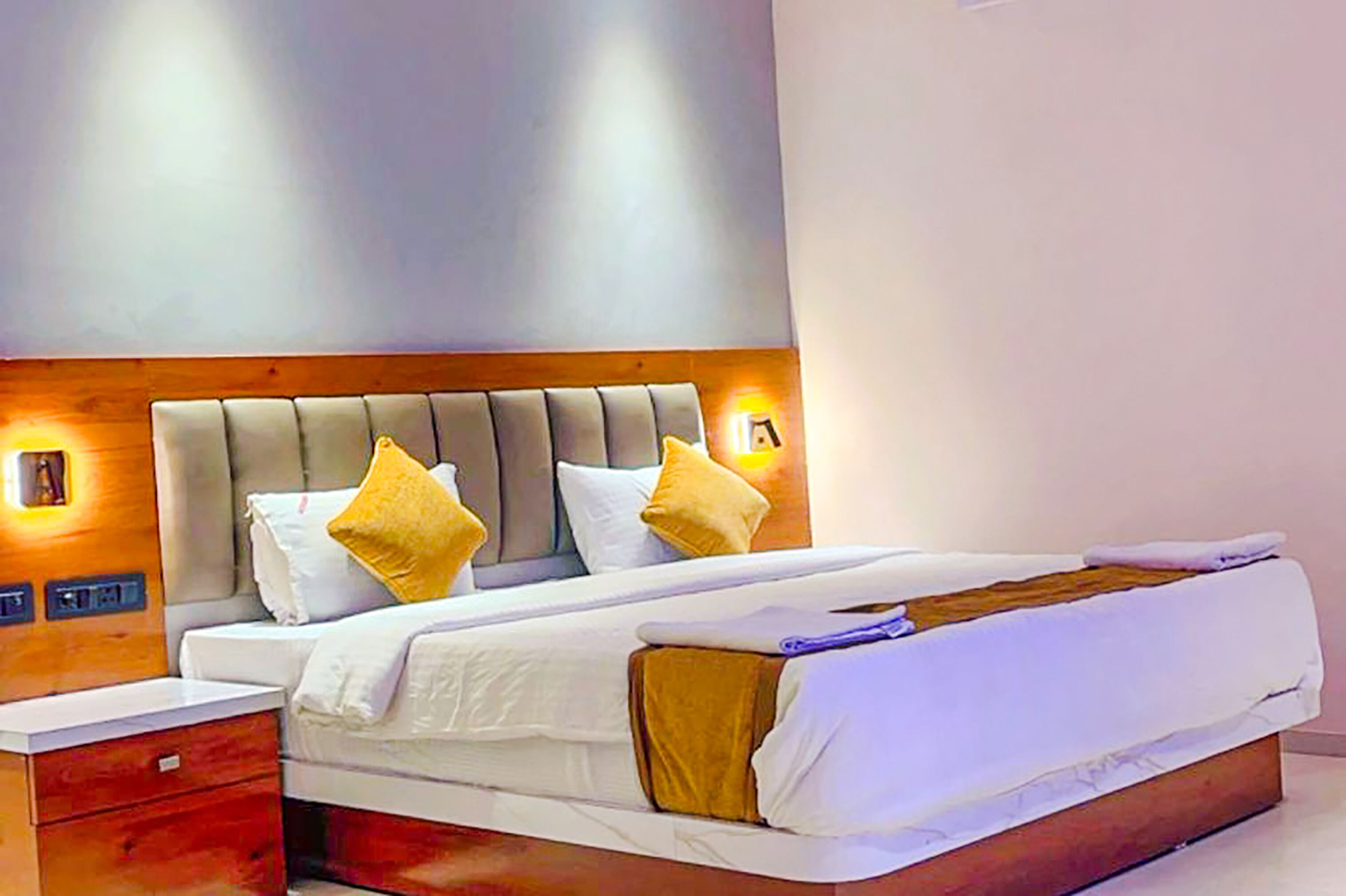 A modern hotel room with a large bed, wooden headboard, and bedside lamps.