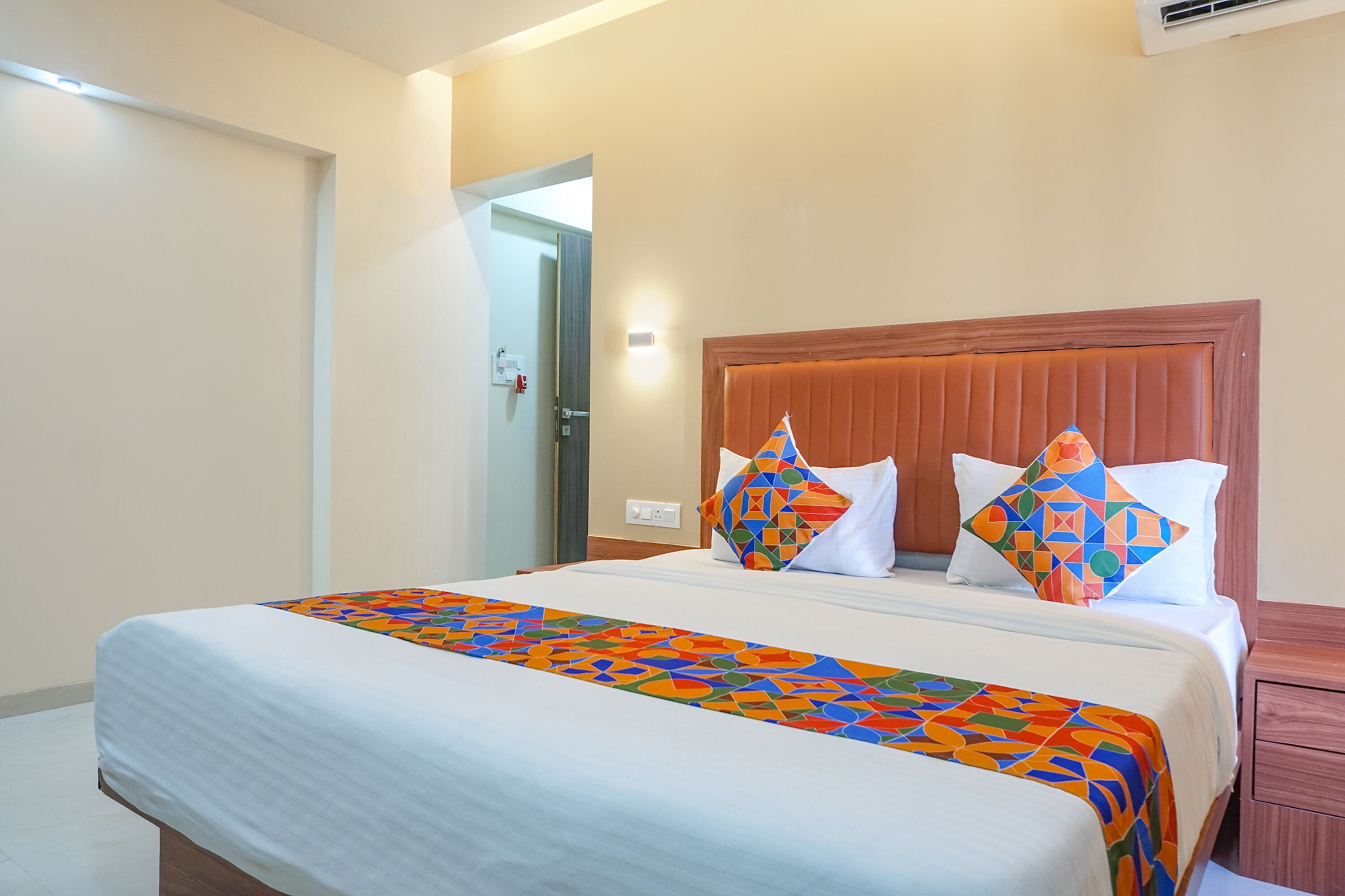 A neatly made bed with a colorful geometric-patterned bedspread, a wooden headboard, and two pillows with a geometric design.