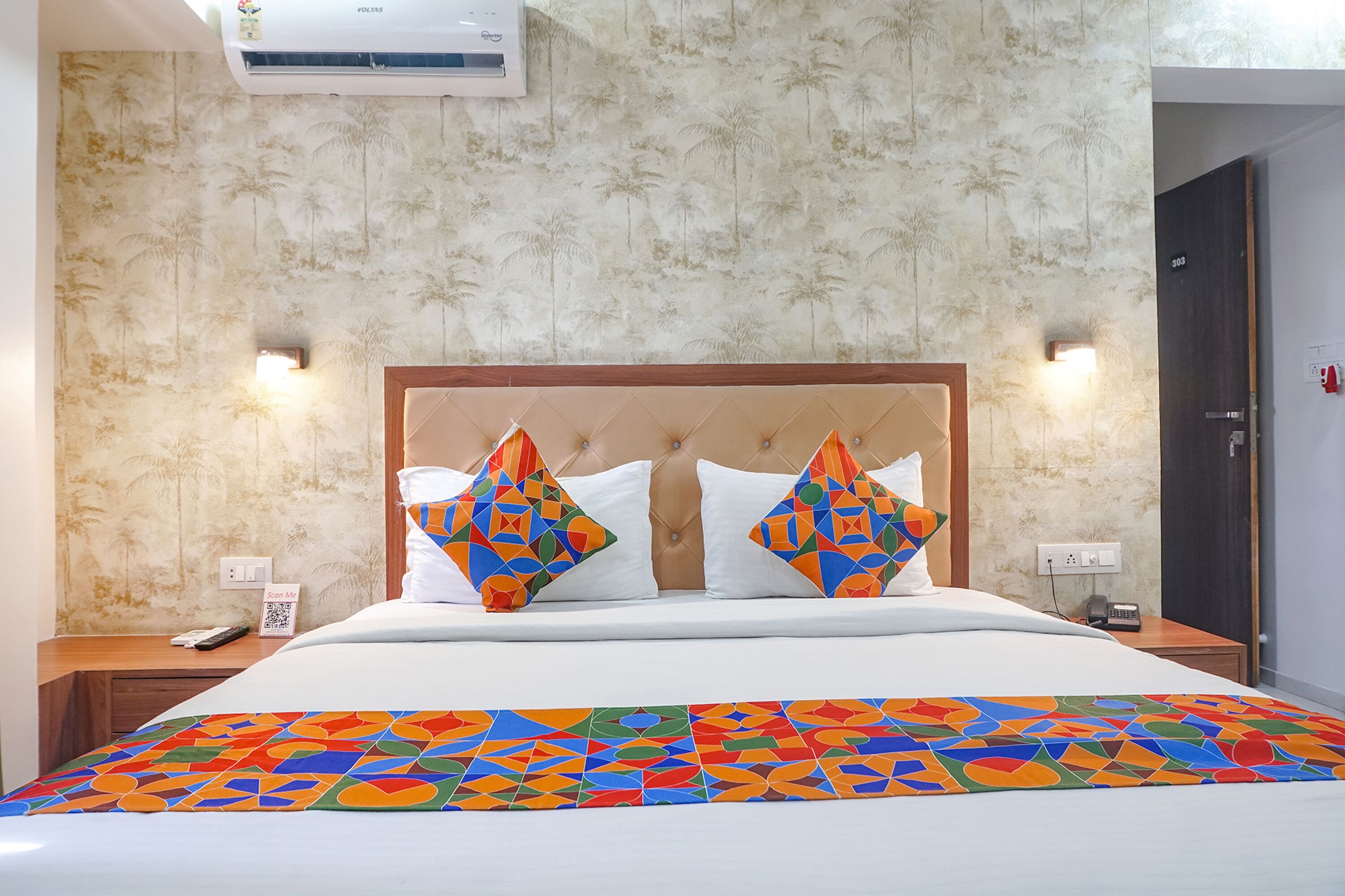 A hotel room with a bed, a headboard, a wall-mounted air conditioner, and a door.
