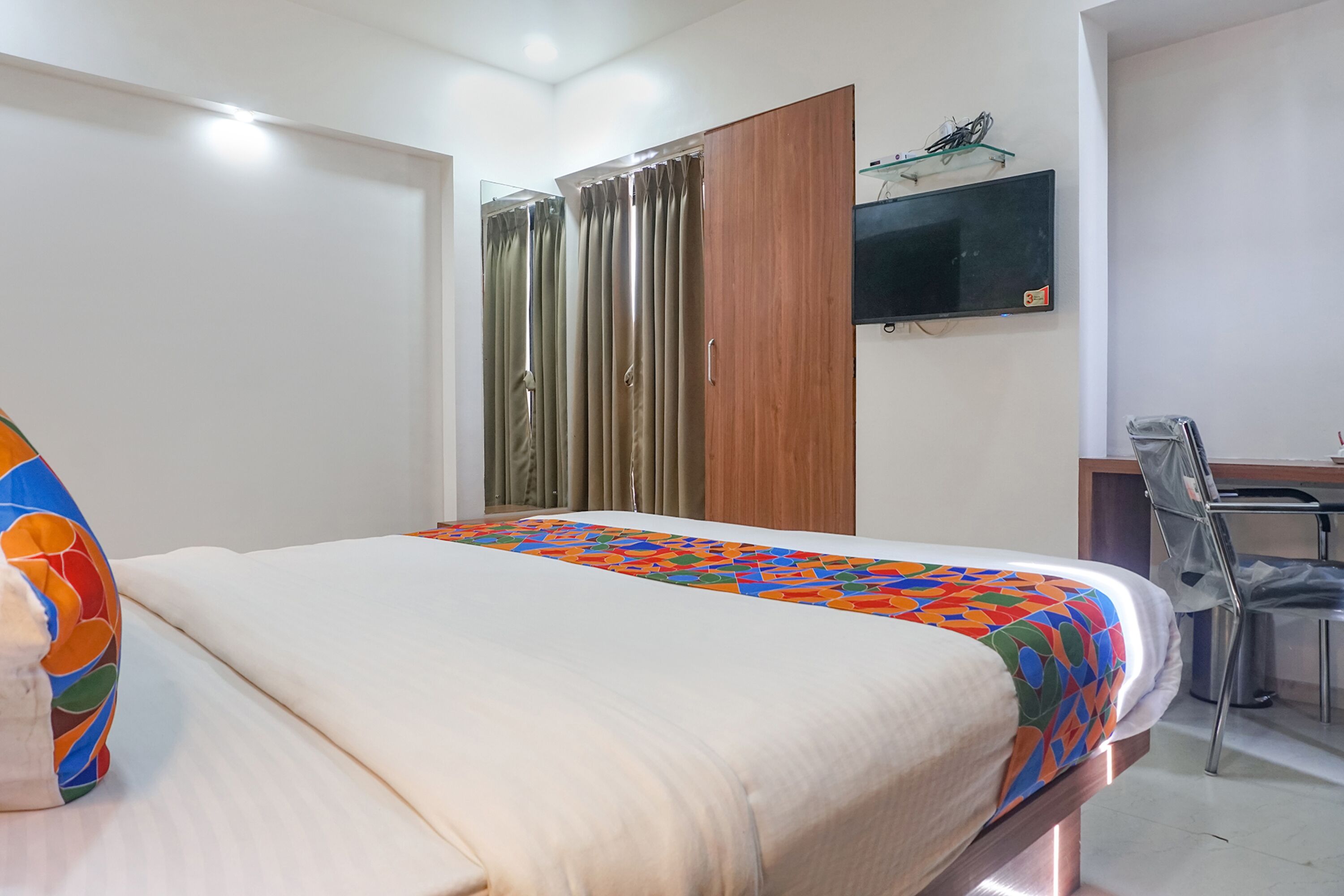 A hotel room with a bed, a desk, a chair, a TV, and a wardrobe.