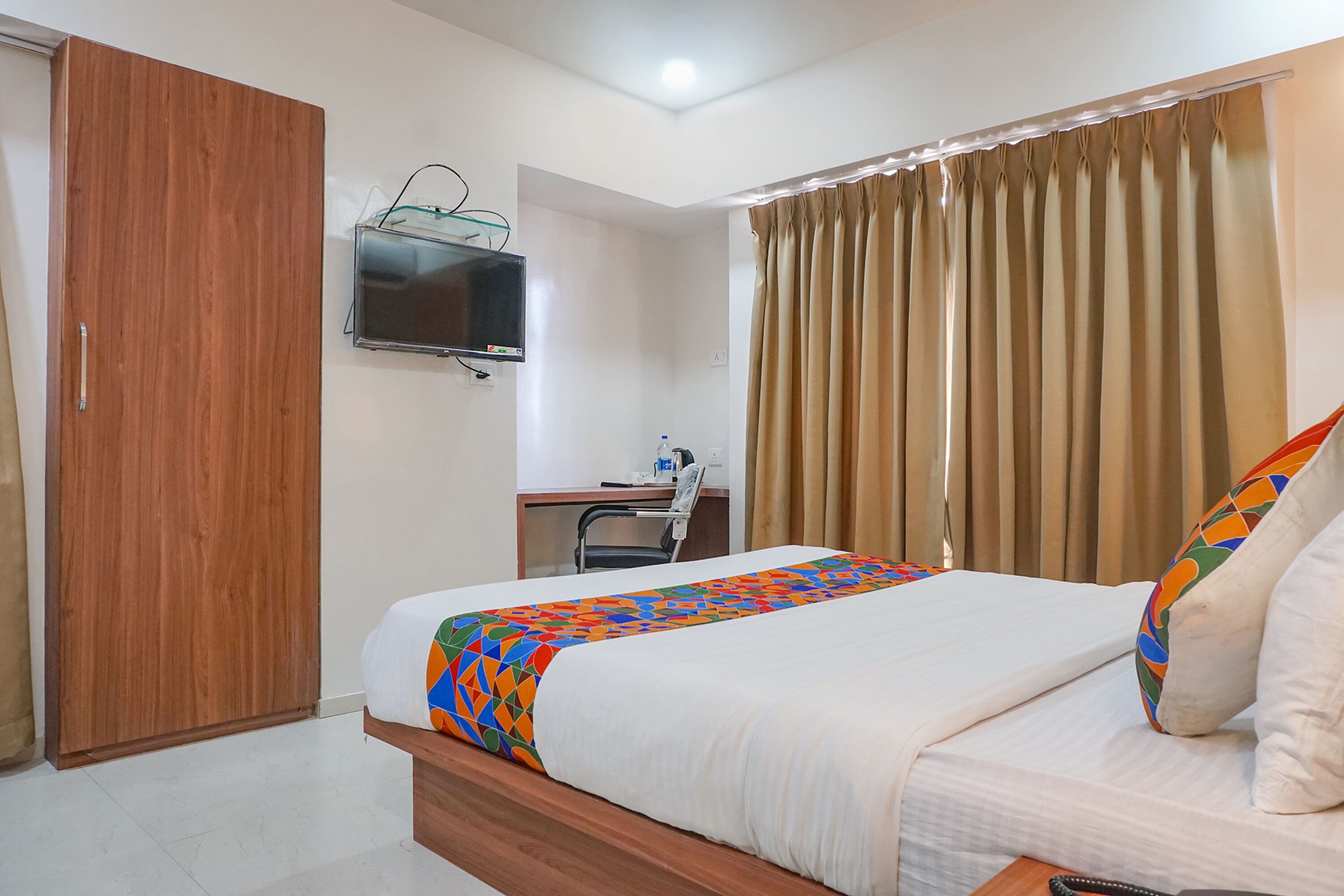 Una habitación de hotel con cama, escritorio, televisión y cortinas.