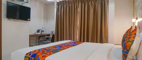 Une chambre d’hôtel comprenant un lit, un bureau avec une chaise, un téléviseur fixé au mur et une fenêtre avec des rideaux.