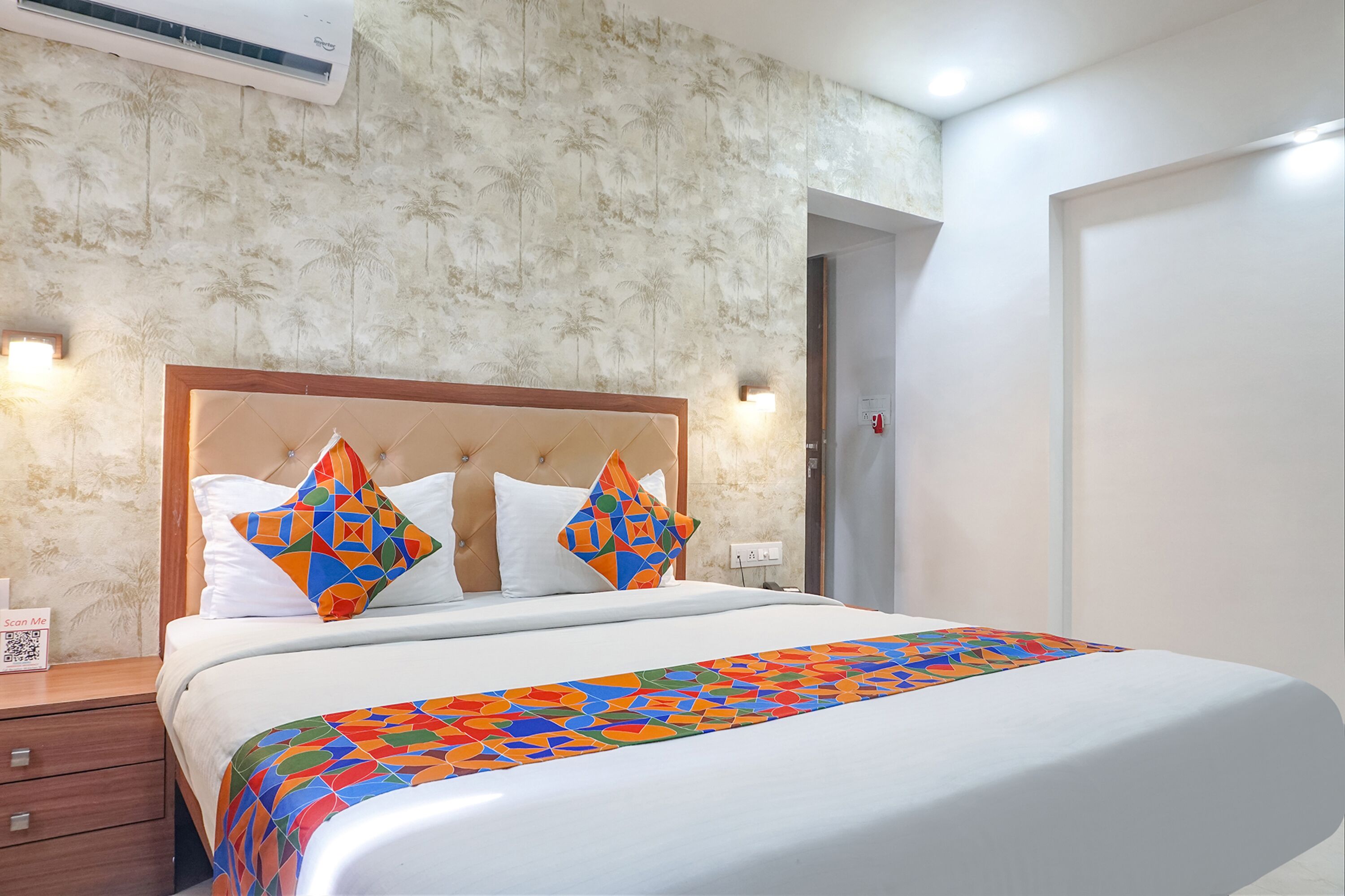 A hotel room with a bed, a nightstand, a wall-mounted air conditioner, and a door.