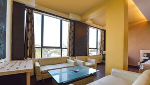 A modern hotel room with a sofa, armchairs, a glass coffee table, and large windows with curtains. - FabHotel Apex Intercontinental - Nr. Pink Square Mall (Jaipur)