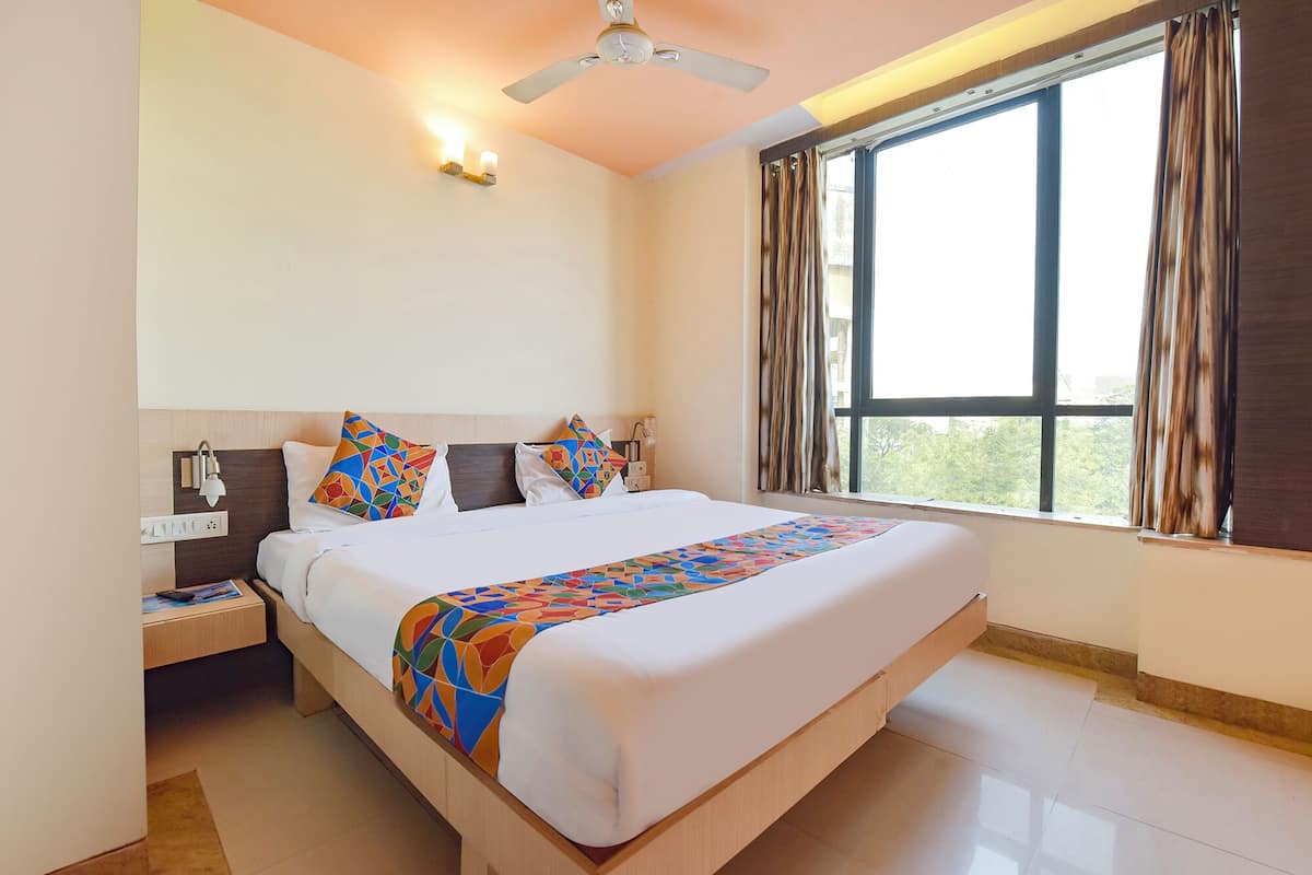 A hotel room with a large bed, a ceiling fan, a nightstand, a lamp, and a window with curtains.