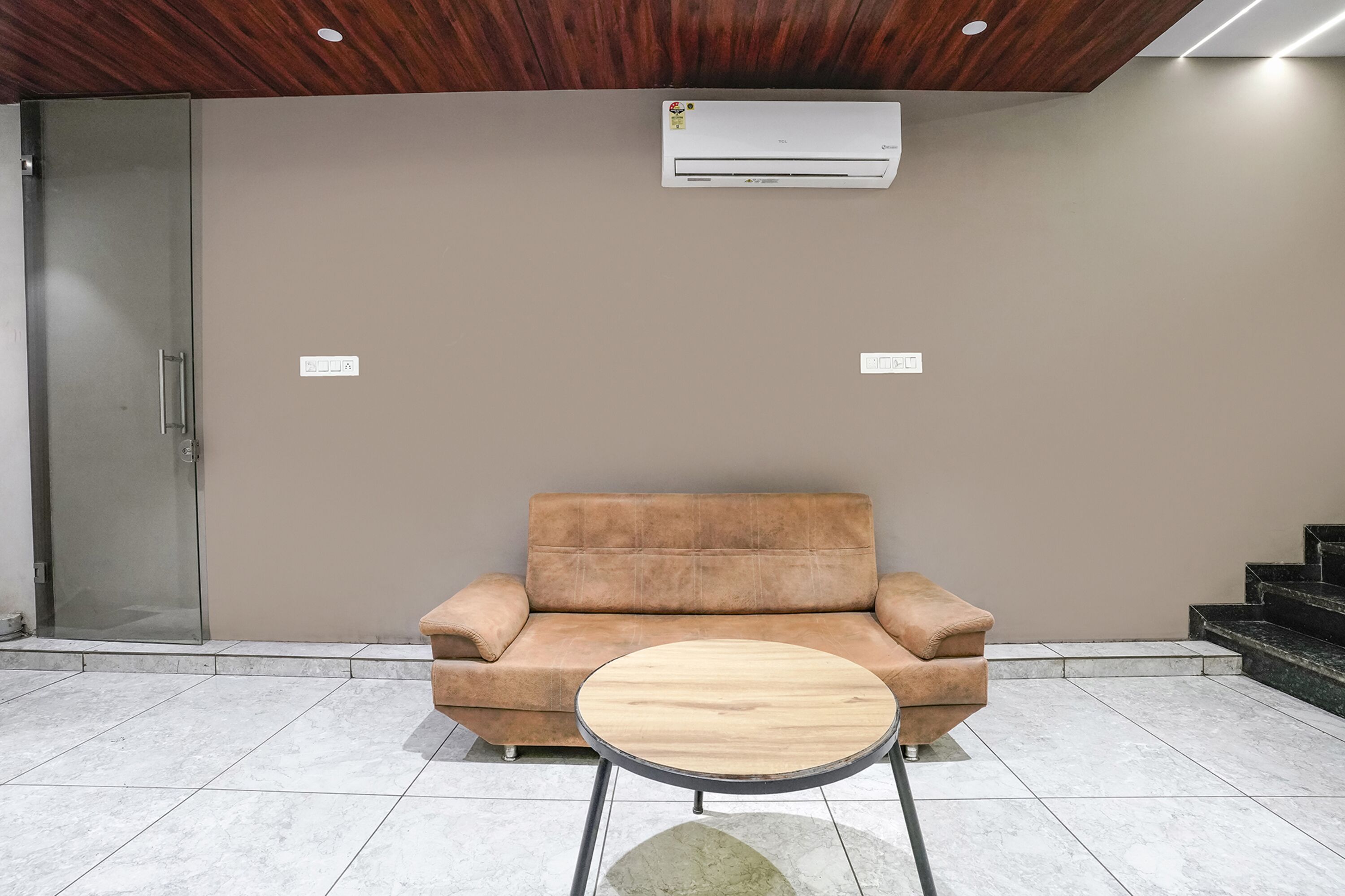 A modern waiting area with a beige sofa, a round wooden table, and a glass door.