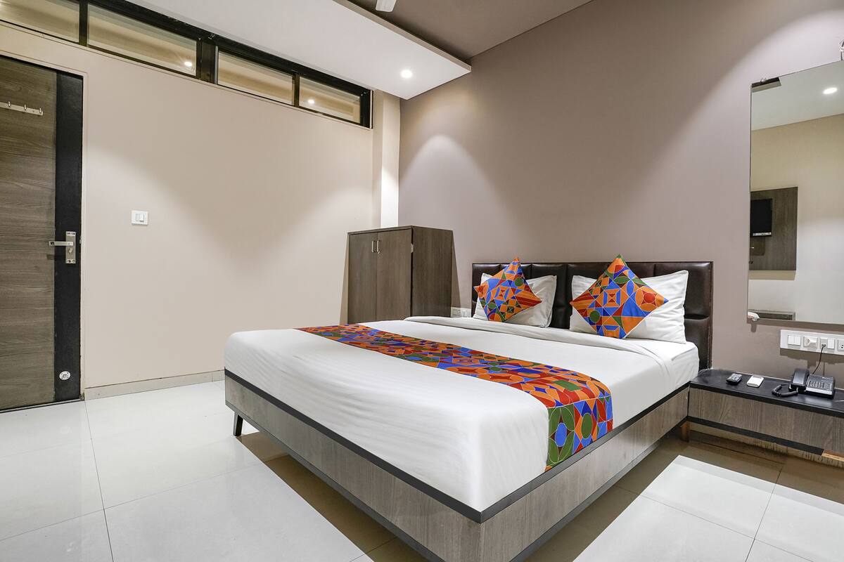 A modern bedroom with a large bed, a wardrobe, a bedside table with a phone, and a mirror on the wall.