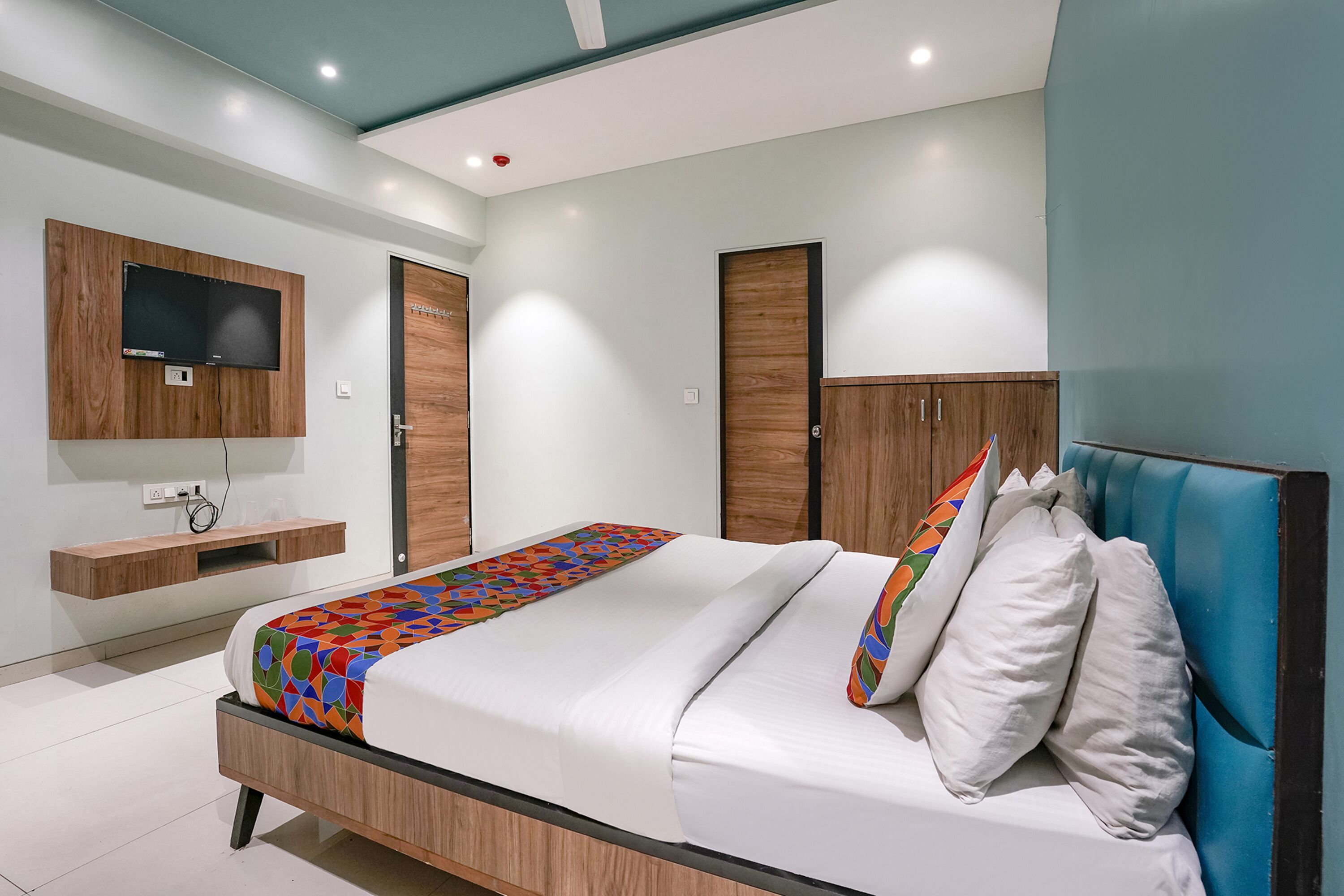 A modern bedroom with a bed, a mounted TV, wooden wardrobe, and a built-in shelf.