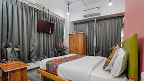 A hotel room with a bed, a wooden nightstand, a TV mounted on the wall, and a wardrobe. - Fabhotel Sky City (Surat)