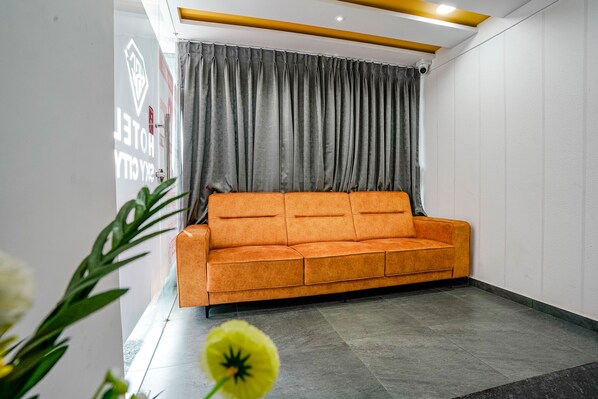 Un hall d’hôtel moderne avec un grand canapé orange, des rideaux gris et un panneau indiquant la vue sur l’hôtel et la ville.