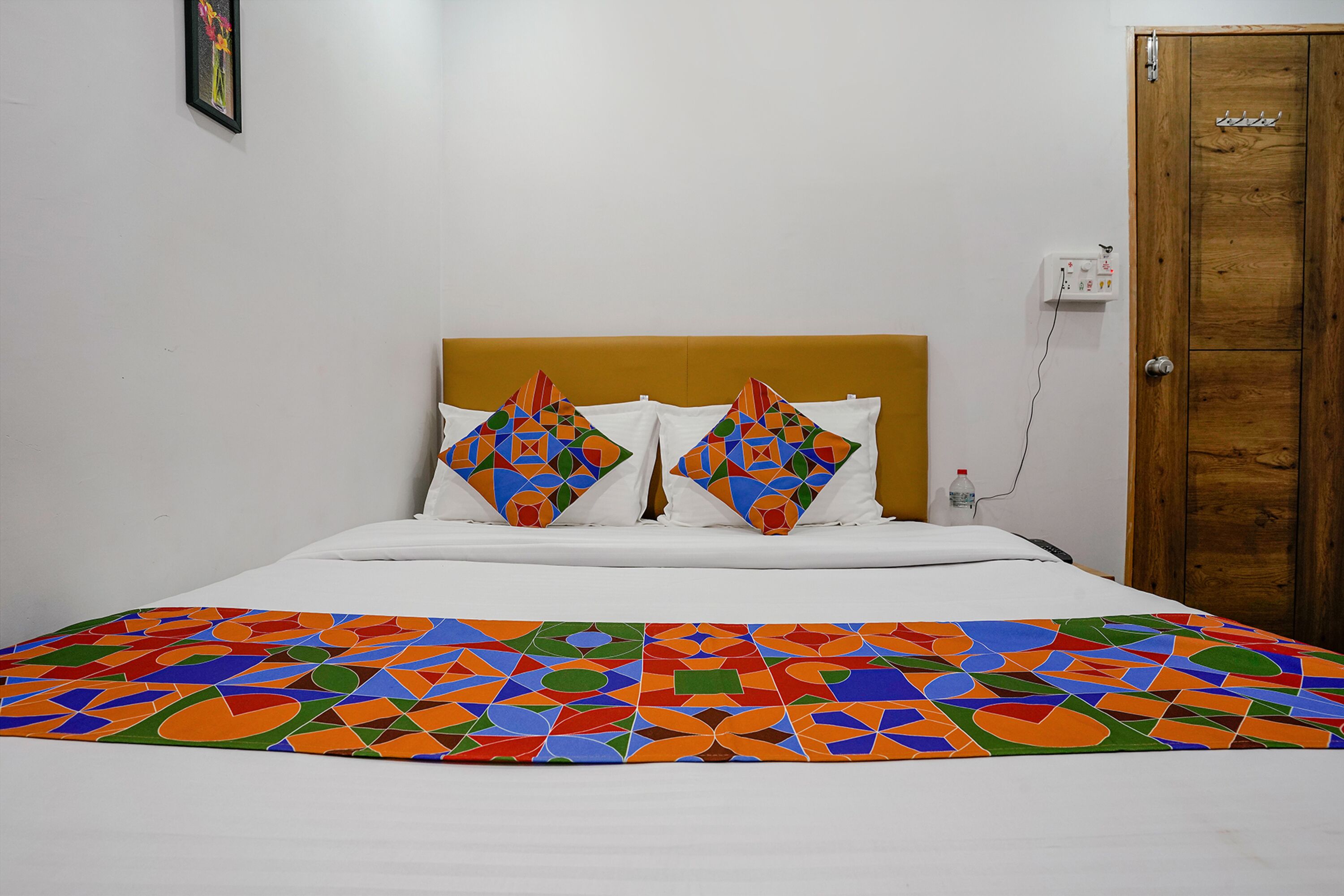Una cama con un edredón de estampado geométrico colorido, un cabecero de madera y dos almohadones decorativos.