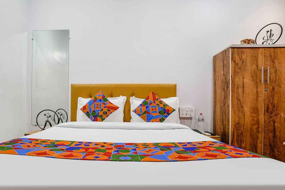 Quarto de hotel com cama, guarda-roupa de madeira e parede branca.