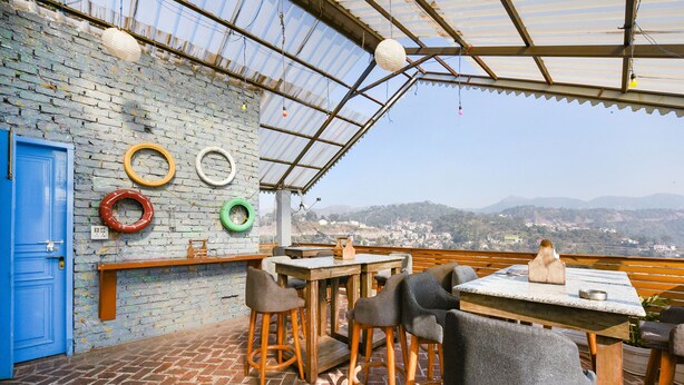 Un bar en la azotea con suelo de ladrillo, muebles de madera y vistas a la ciudad y colinas.