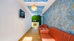 Un espace d’accueil d’hôtel au design moderne, comprenant un comptoir d’accueil, un canapé rouge et un plafond orné d’une fresque représentant des nuages.