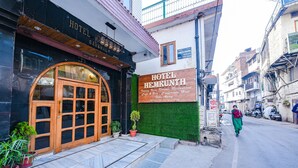 Entrada de un hotel con un gran arco, un cartel con el nombre del hotel y un pequeño jardín con plantas en macetas.