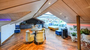 Una habitación moderna estilo loft con techo inclinado, piso de madera, una zona de estar central con mesas y sillas redondas, un sofá y una cocina integrada.