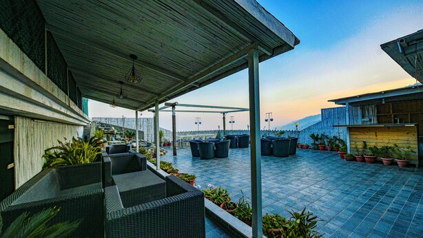 Una terraza en la azotea con mobiliario exterior, plantas en macetas y vistas de la ciudad.