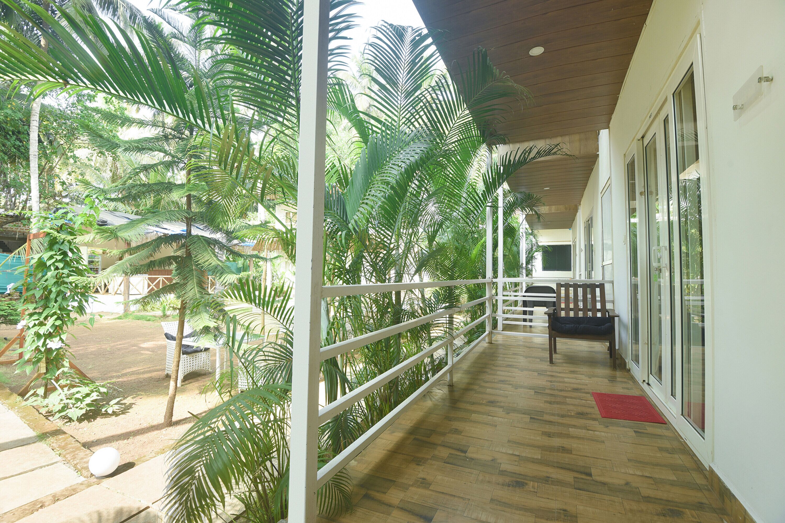 A covered balcony with wooden flooring, white railings, and a bench.