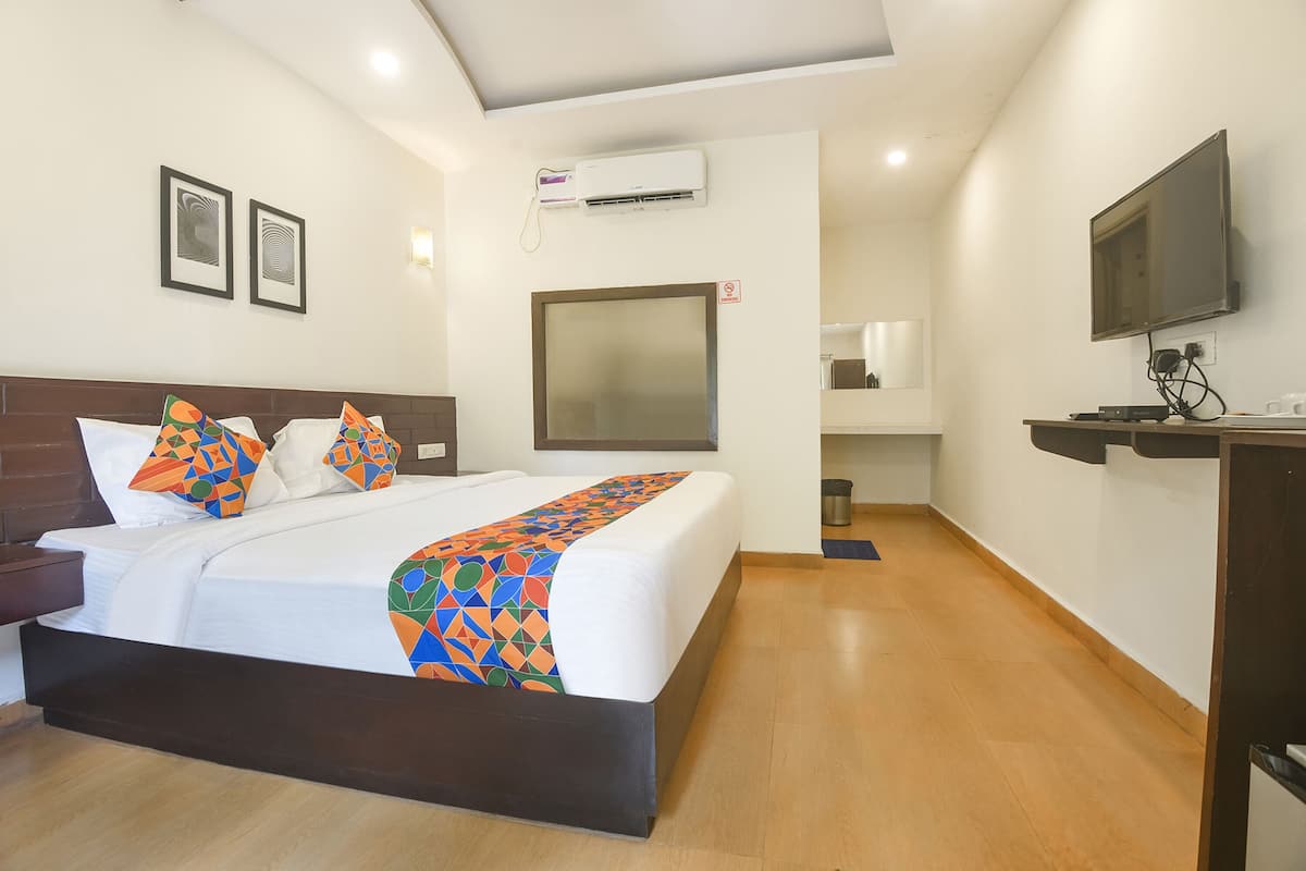 A hotel room with a bed, a TV, an air conditioning unit, and a desk with a computer.