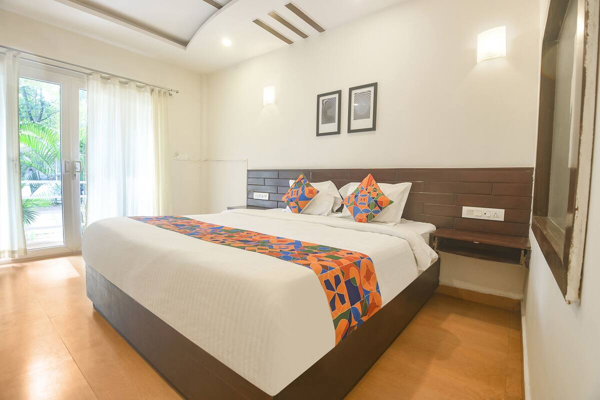 A hotel room with a large bed, a nightstand, a wall-mounted TV, and a window with curtains.