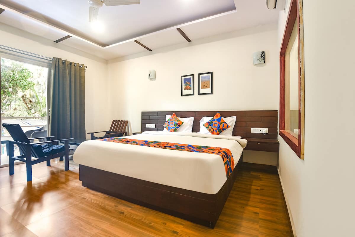 A hotel room with a large bed, a chair, a desk, and a window with curtains.