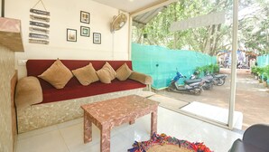 A room with a red sofa, a marble table, and a large window with a view of parked scooters and greenery outside. - Fabhotel La Volga (Morjim)