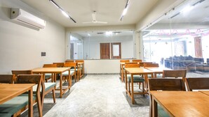 A conference room with wooden tables and chairs, a ceiling fan, and an air conditioning unit. - Fabexpress Rs Villa (Barasat)