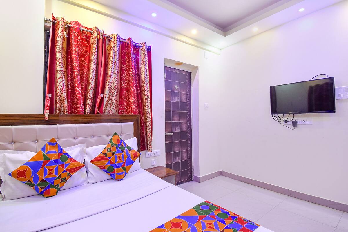 A hotel room with a bed, colorful pillows, a TV, and a shower area.
