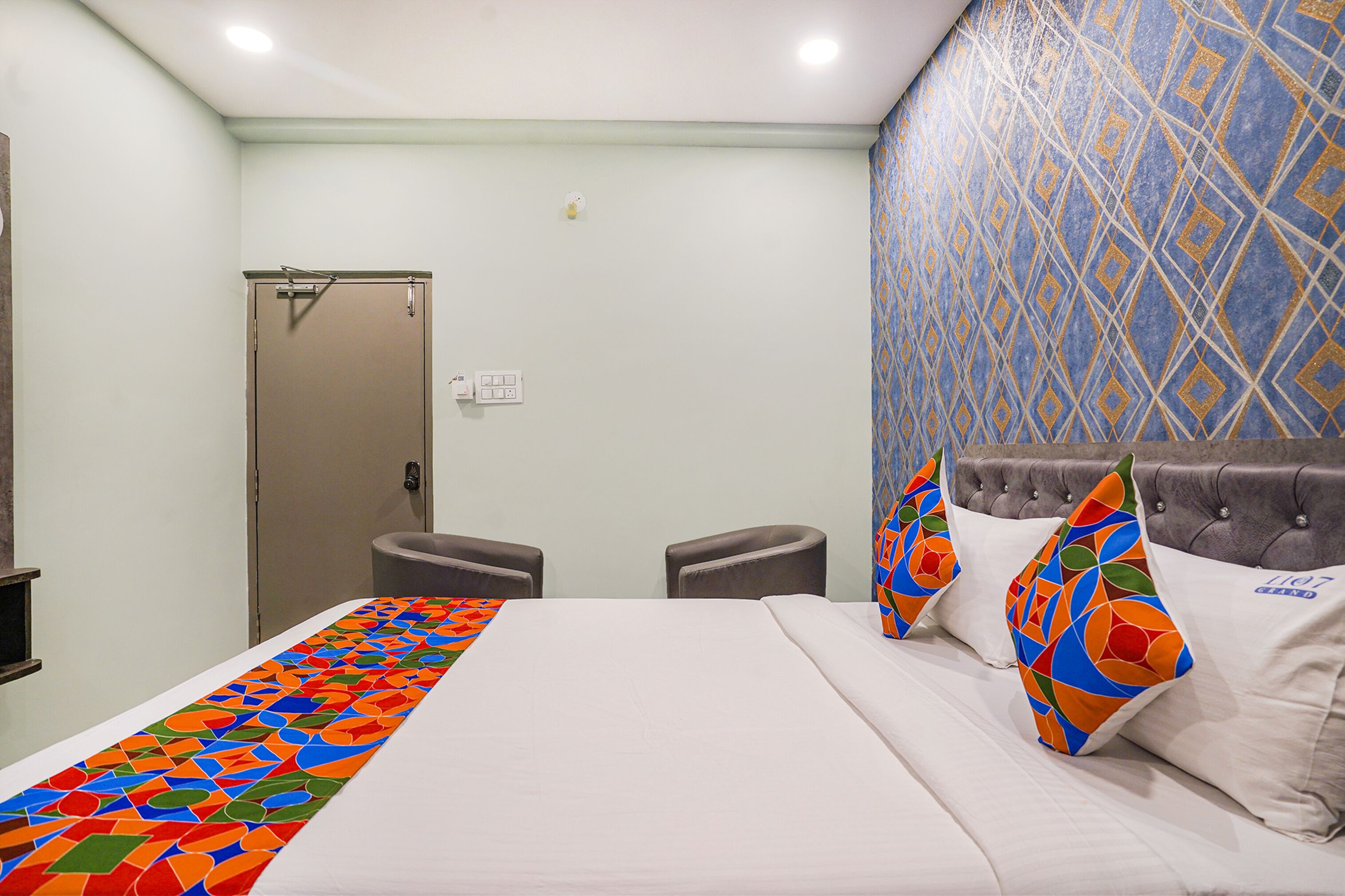 Une chambre d’hôtel avec un lit, deux chaises, une table de chevet et un mur décoré d’un motif.