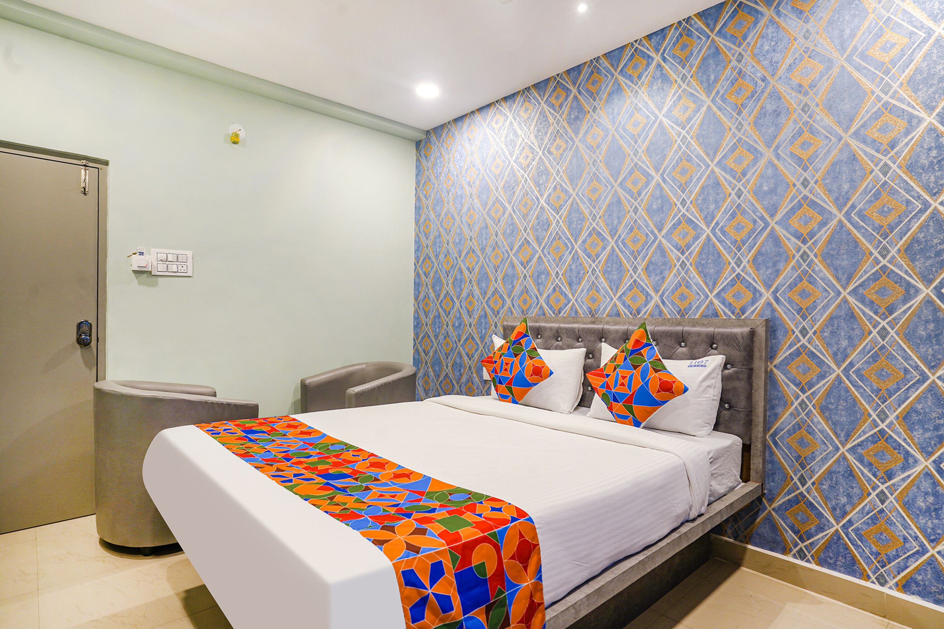 A hotel room with a bed, a bedside table, a trash bin, and a wall with a geometric pattern.
