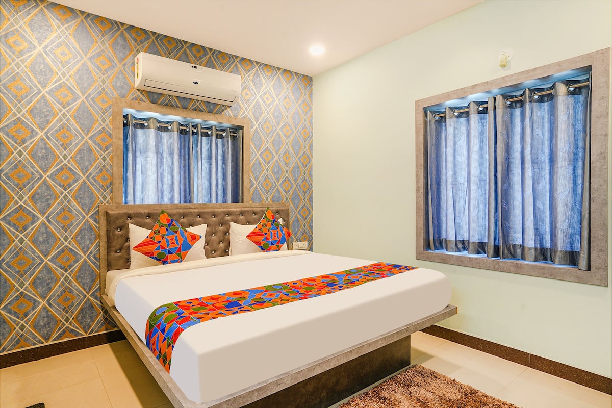 Quarto com cama, papel de parede estampado, aparelho de ar condicionado, janela com cortinas e cabeceira.