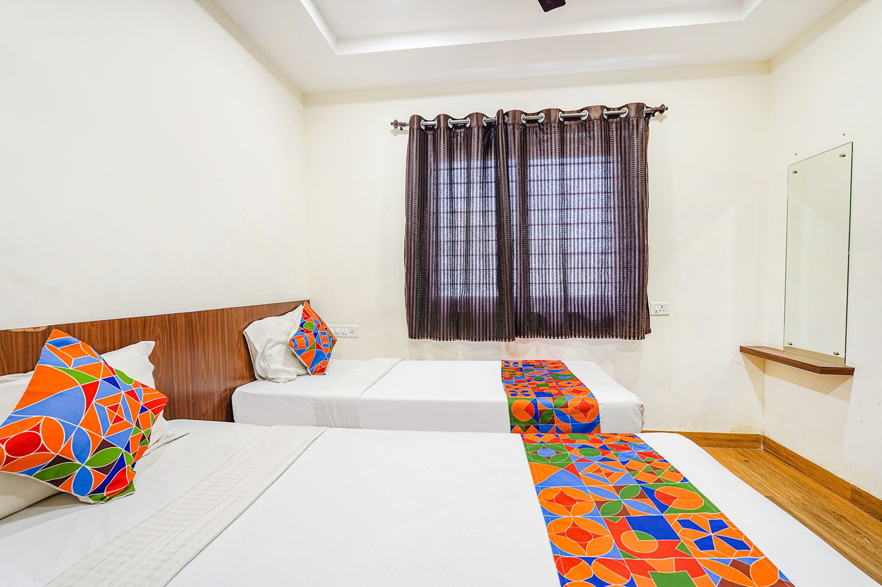 A hotel room with two beds, a large mirror, and a window with curtains.