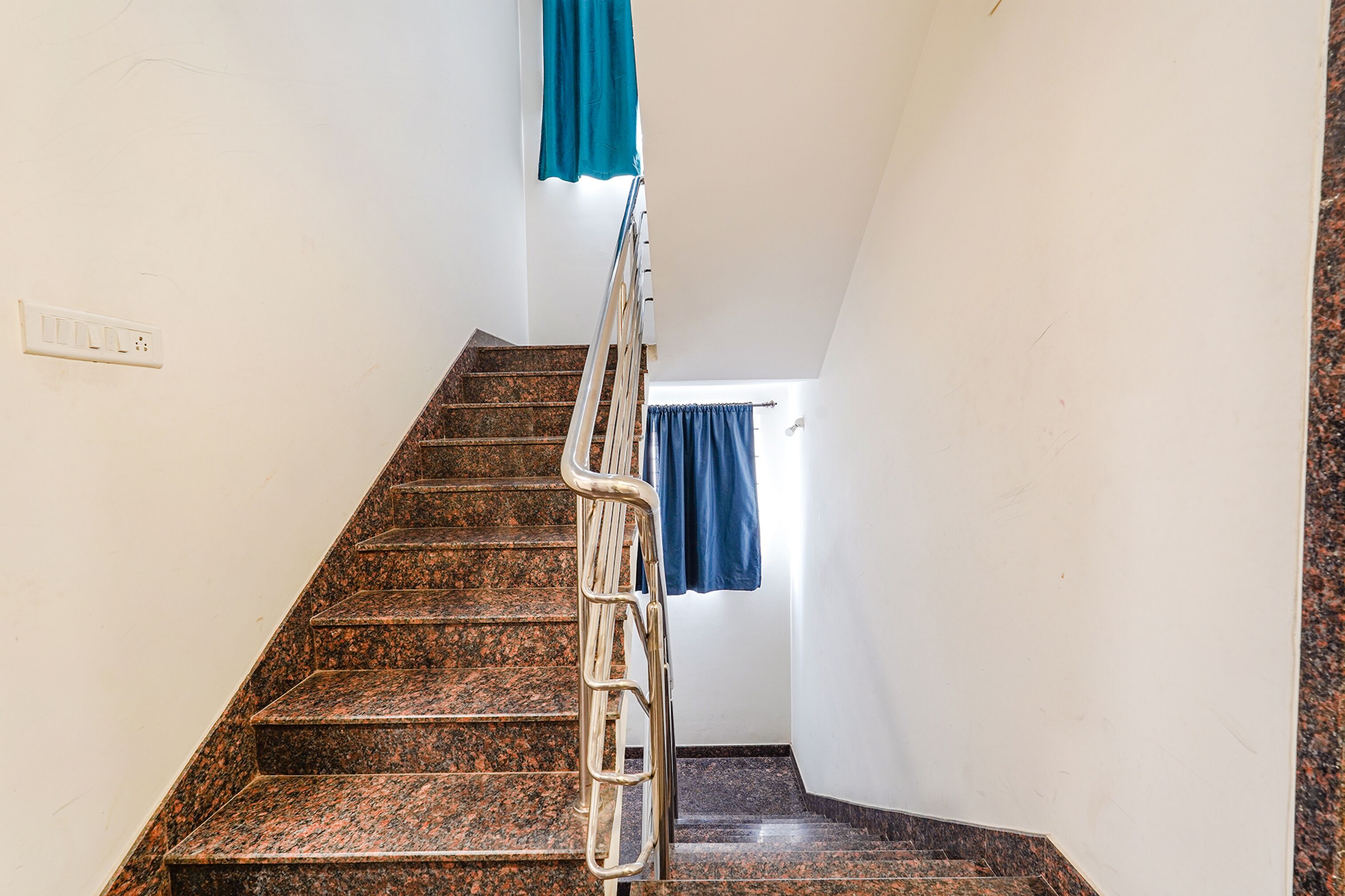 Una escalera con barandilla de metal, un enchufe en la pared y una cortina azul en la parte superior.