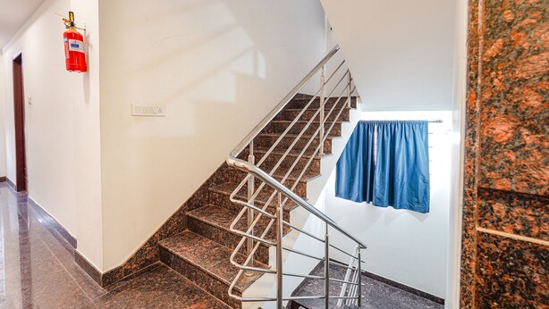 A staircase with a metal handrail, a fire extinguisher mounted on the wall, and a blue curtain hanging on the right side. - Fabexpress Symphony Suites (Bengaluru)