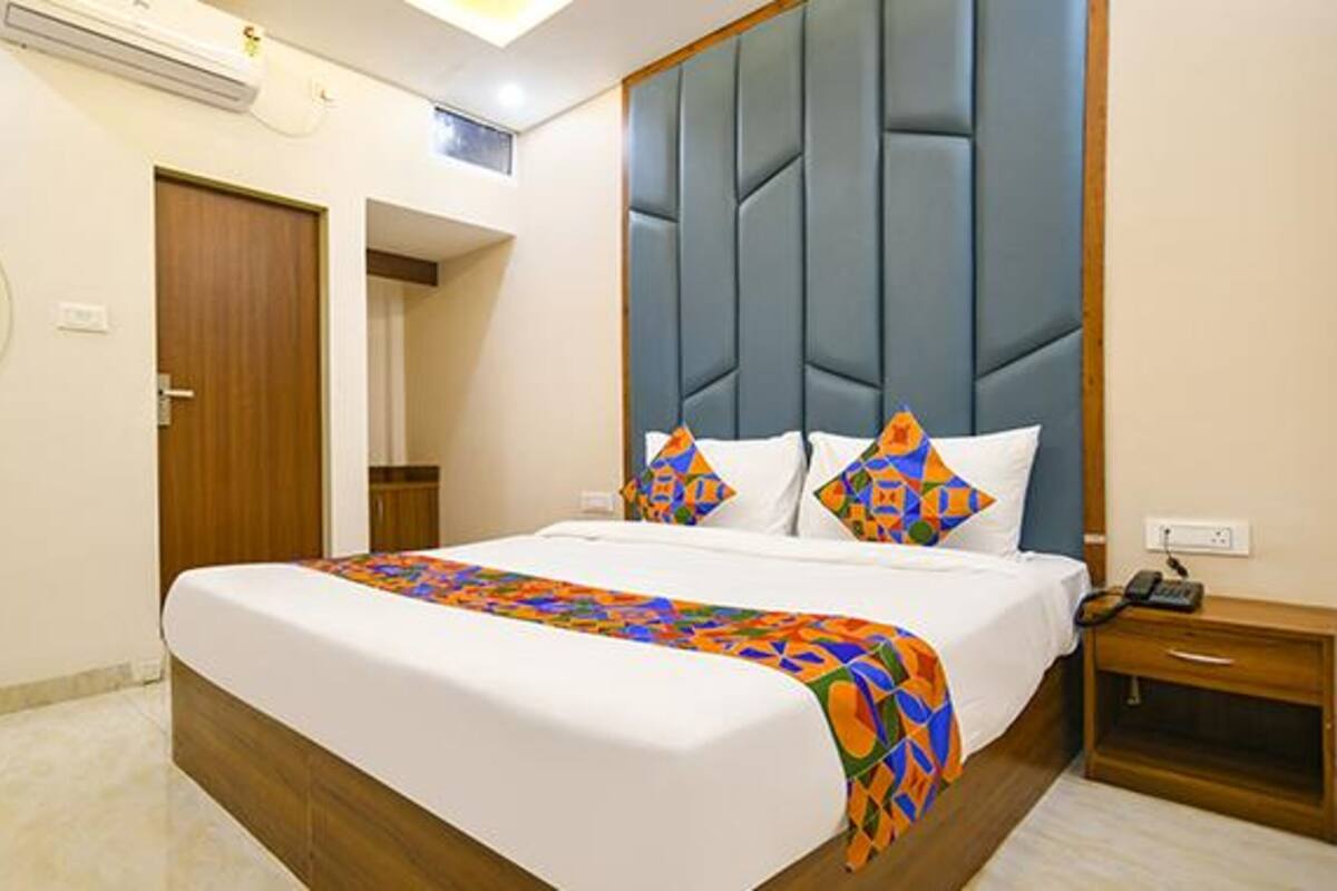 A hotel room with a large bed, a wooden headboard, a bedside table, and a mirror on the wall.