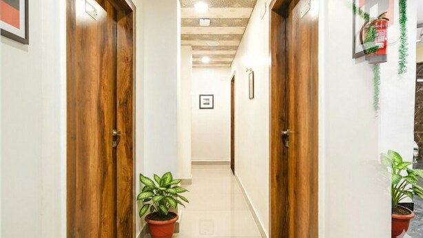 A narrow hallway with wooden doors, potted plants, and a fire extinguisher on the wall. - FabHotel The King Palace (Indore)