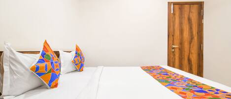 Habitación de hotel con cama, ropa de cama blanca, almohadas coloridas, una puerta de madera y un corredor de cama estampado.