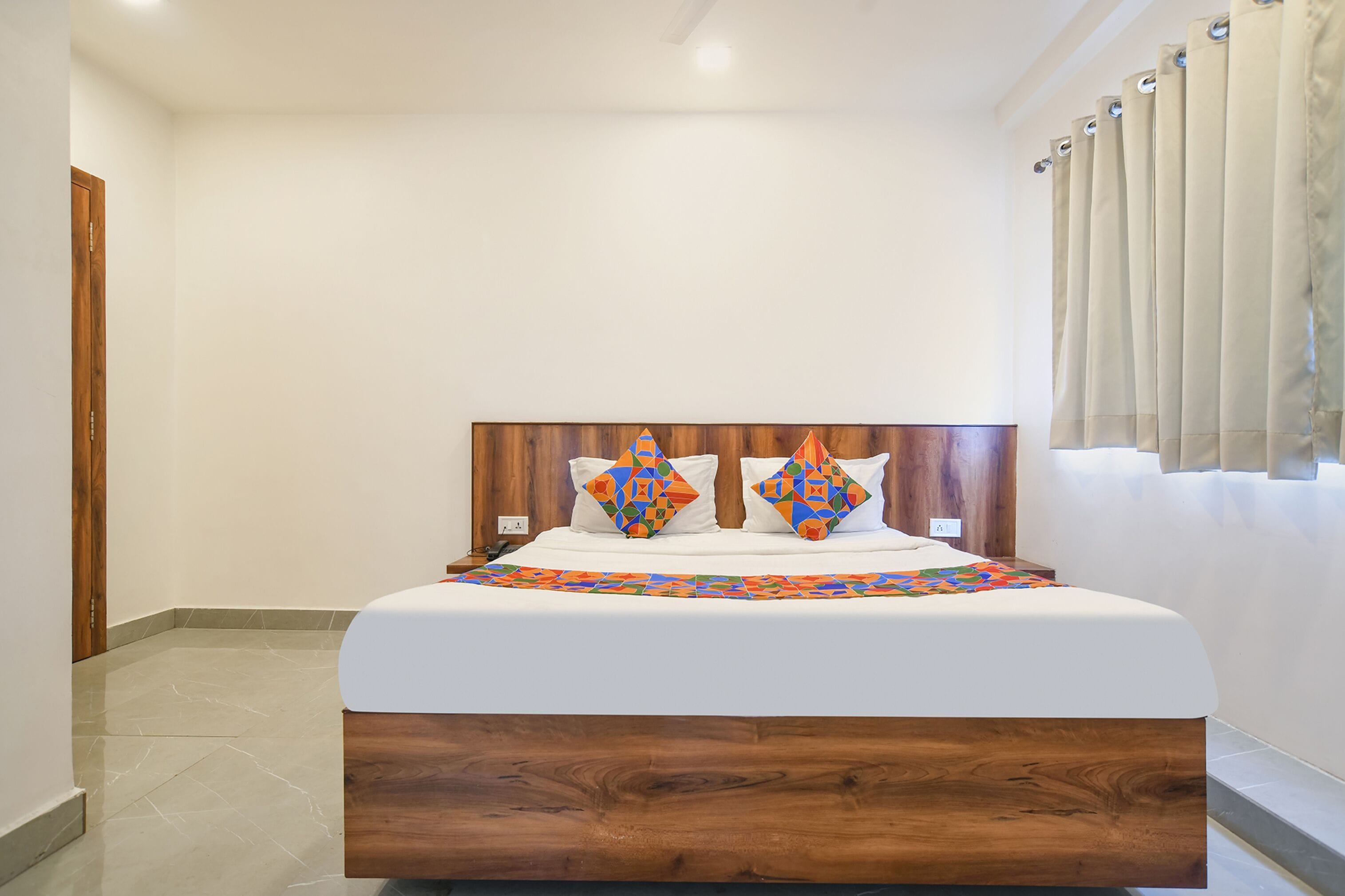 Una cama bien tendida con un cabecero de madera, una colcha estampada y dos almohadones decorativos.