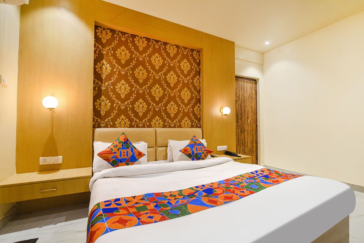 A hotel room with a large bed, two bedside tables, a wooden headboard, and patterned wallpaper.