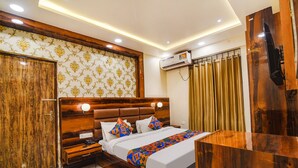 A hotel room with a wooden headboard, a bed with patterned pillows, a bedside table with a lamp, an air conditioning unit, and a TV mounted on the wall. - FabHotel Icon (Danapur)